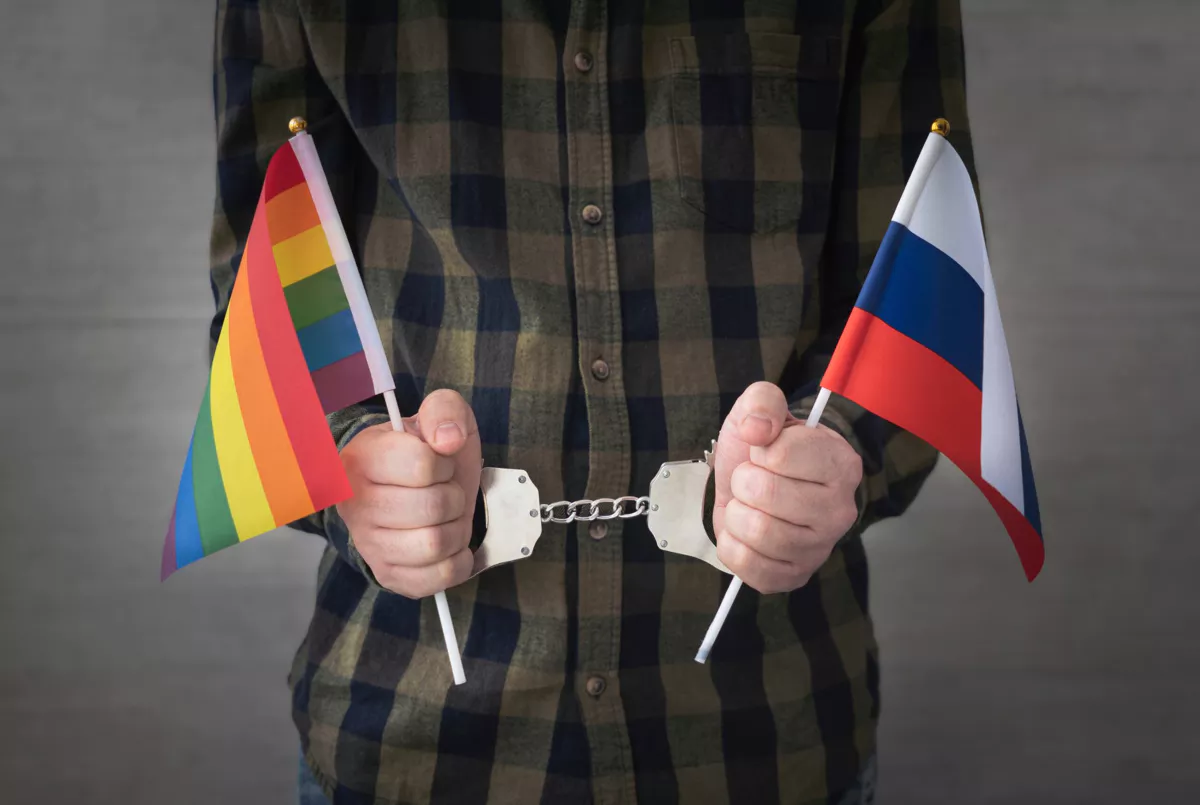 Un homme menotté tient un drapeau russe et un drapeau de la fierté.