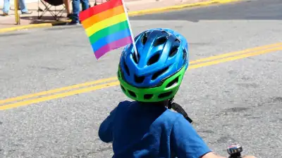 Jeune enfant à bicyclette portant un casque avec le drapeau arc-en-ciel